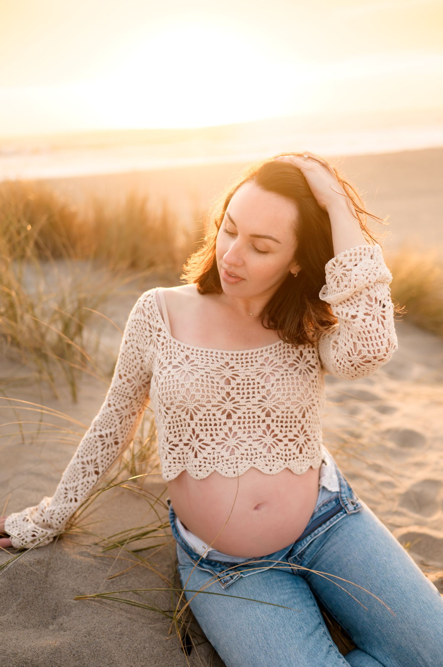 woman in crochet crop top shows bare belly during Ventura beach sunset maternity photoshoot by Ventura maternity photographer