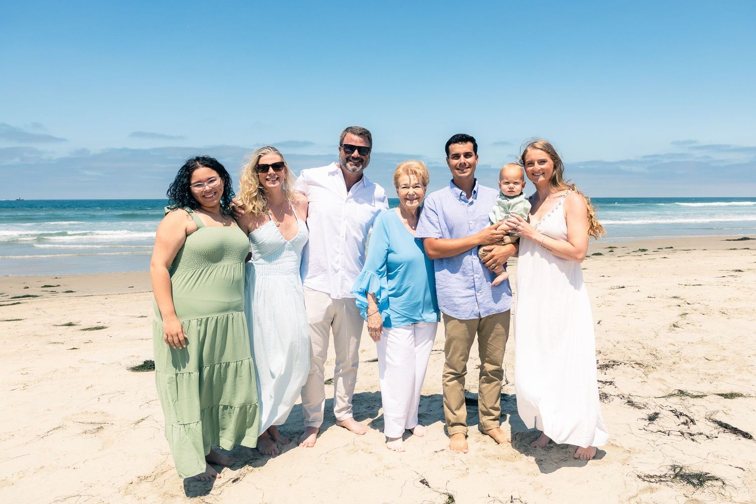 San Diego family portrait photography of a multi-generational family posing on a sunny beach with the ocean waves behind them.