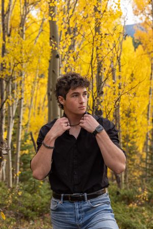 Person in a black button-down shirt and jeans poses against vibrant yellow fall foliage in an aspen forest.