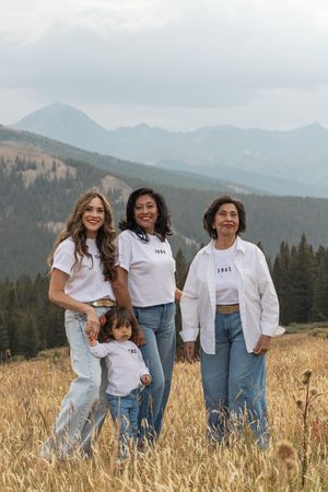 A group in matching white tops and blue jeans pose together in a scenic mountain field with golden grass.