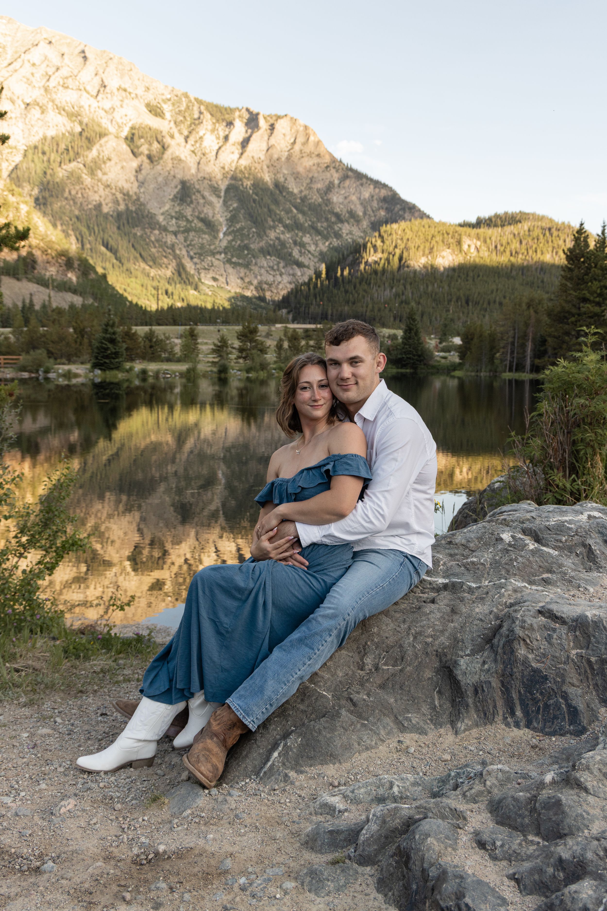 A couple sits on lakeside rocks at sunset with mountain reflections in Officer's Gulch