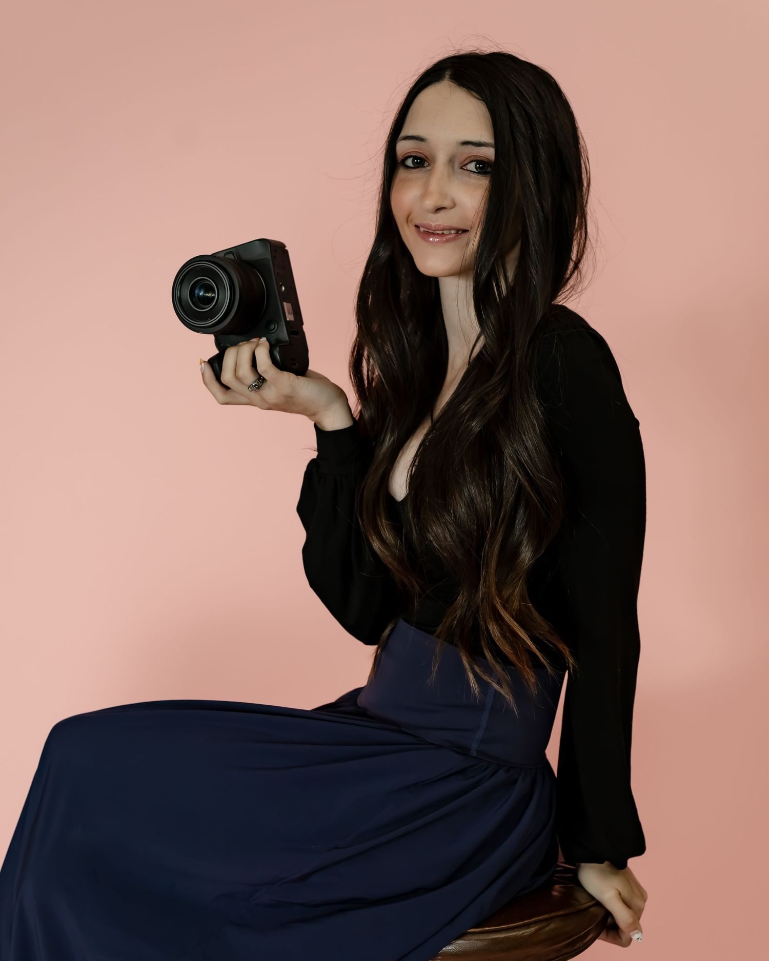 Portrait of woman with long dark hair holding camera against pink background.