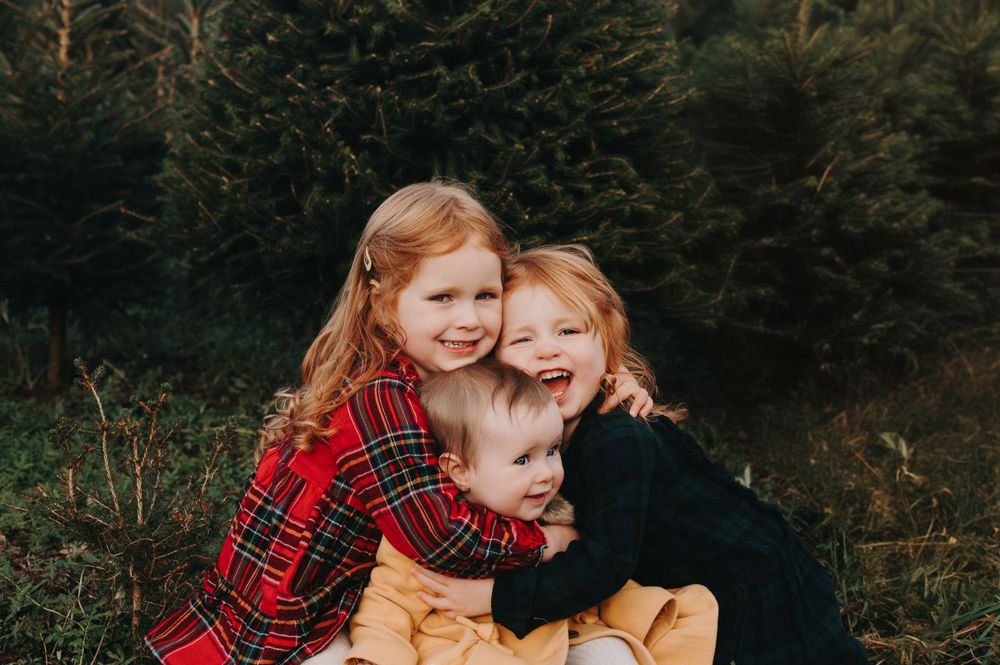 three sisters sitting on grass hugging in dresses
