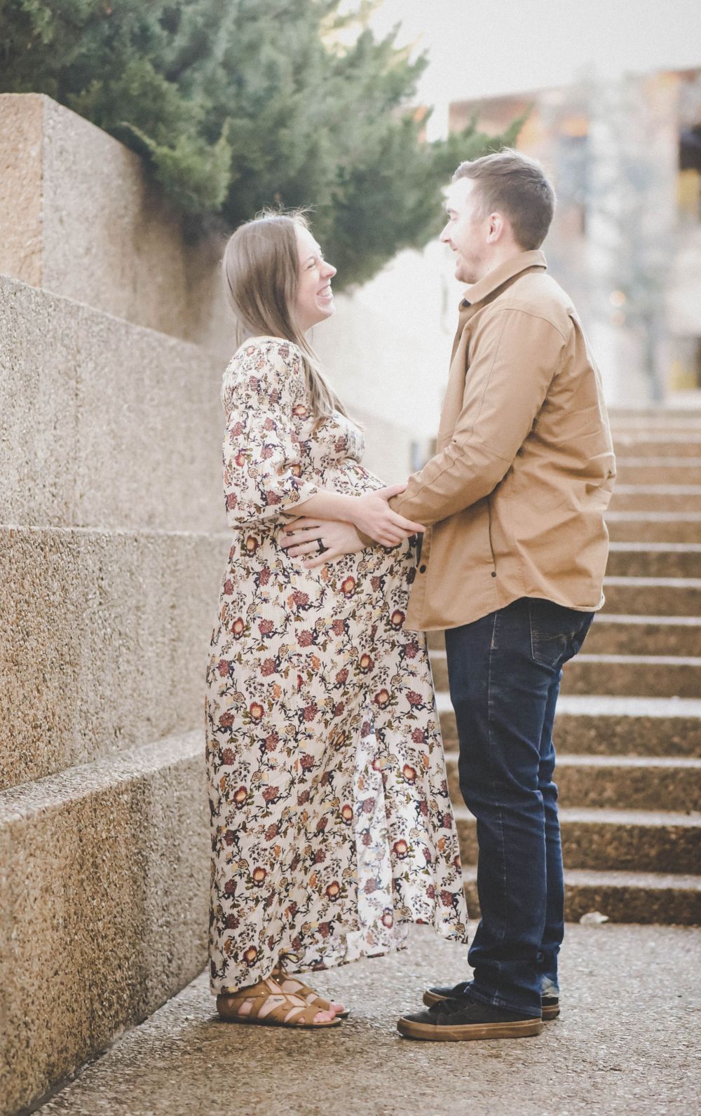 Expecting couple facing each other on stone steps, man gently touching pregnant belly.