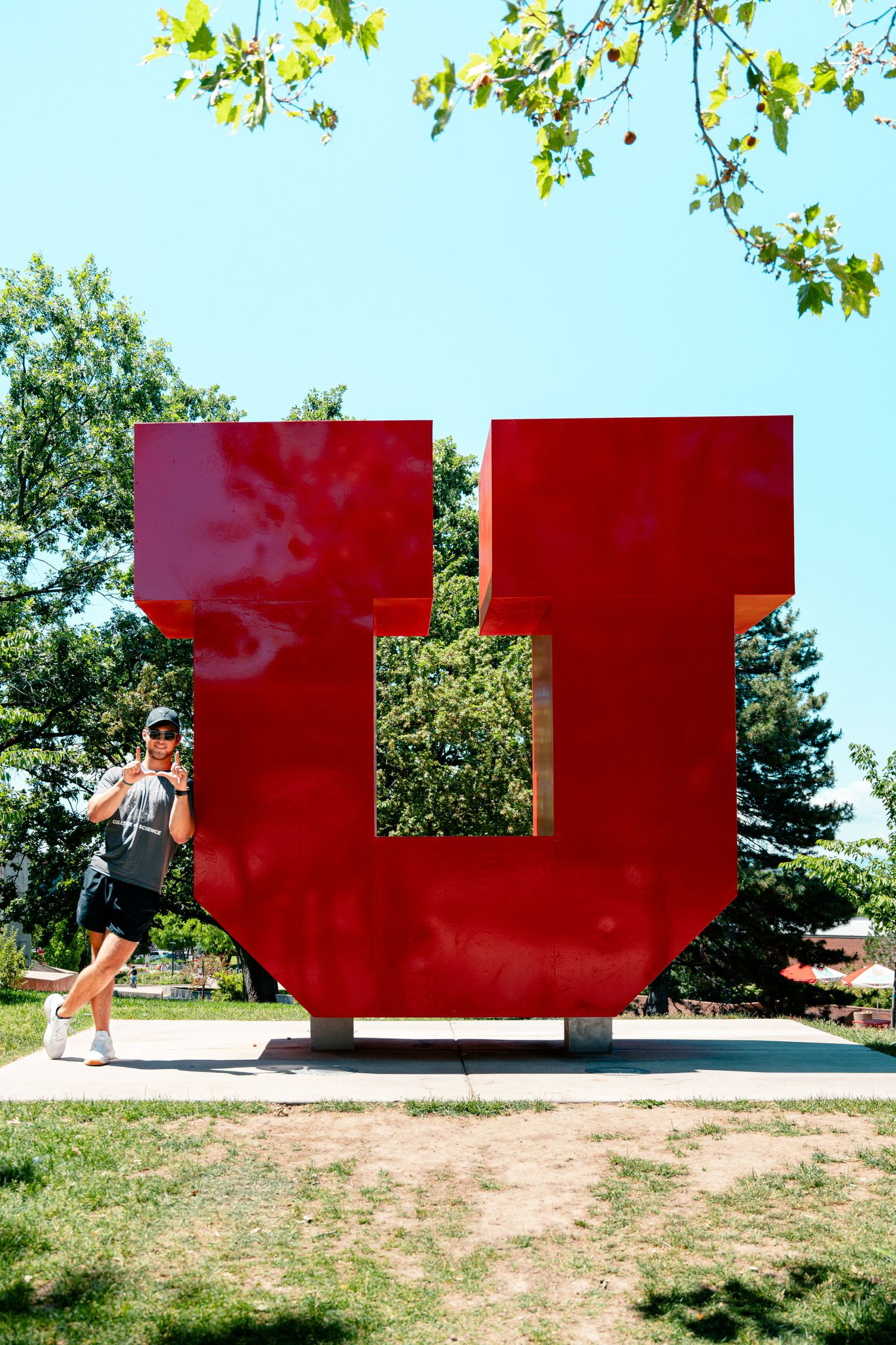 Large red metal 'U' sculpture displayed outdoors against blue sky and trees.
