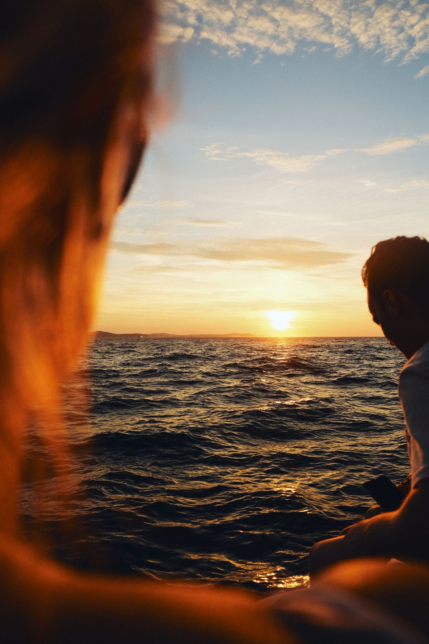 Two silhouettes watching a golden sunset over rippling ocean waves at dusk.