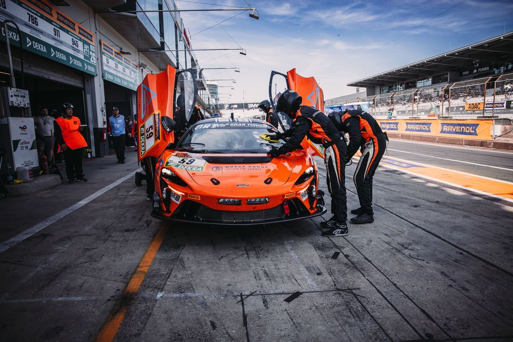 Orange McLaren race car with butterfly doors open being serviced in pit lane at a motorsport racetrack.