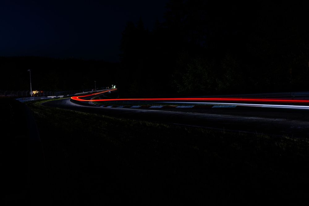 Night time long exposure photo of car light trails winding through a dark mountain road.