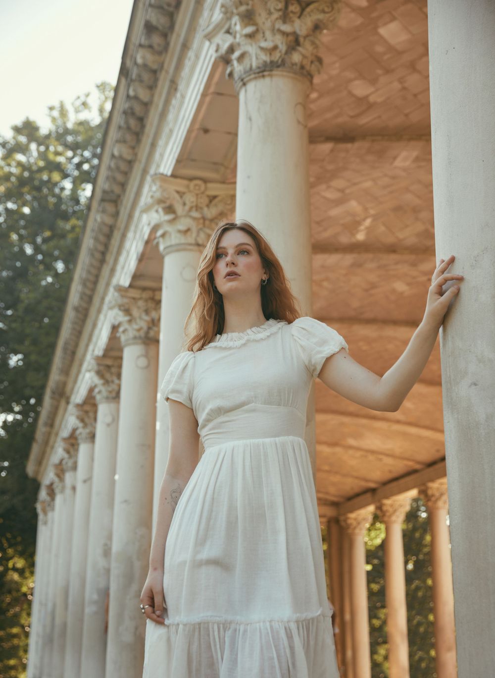 Elegant white dress flowing against classical columns in golden afternoon light.