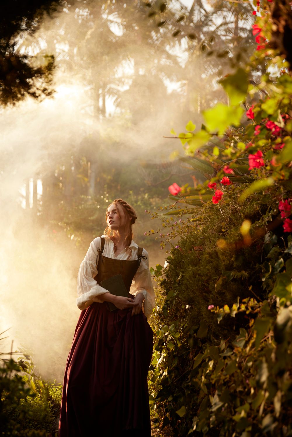 Sunlit garden scene with red flowers and figure in rustic dress standing among climbing vines.