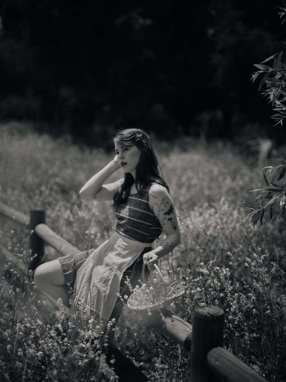 A girl in a vintage dress sits playfully in a wildflower meadow in black and white.