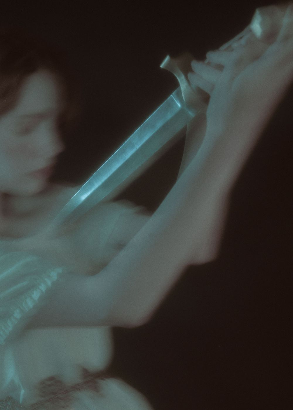 Ethereal blue-tinted image of a hand holding a dagger in motion.