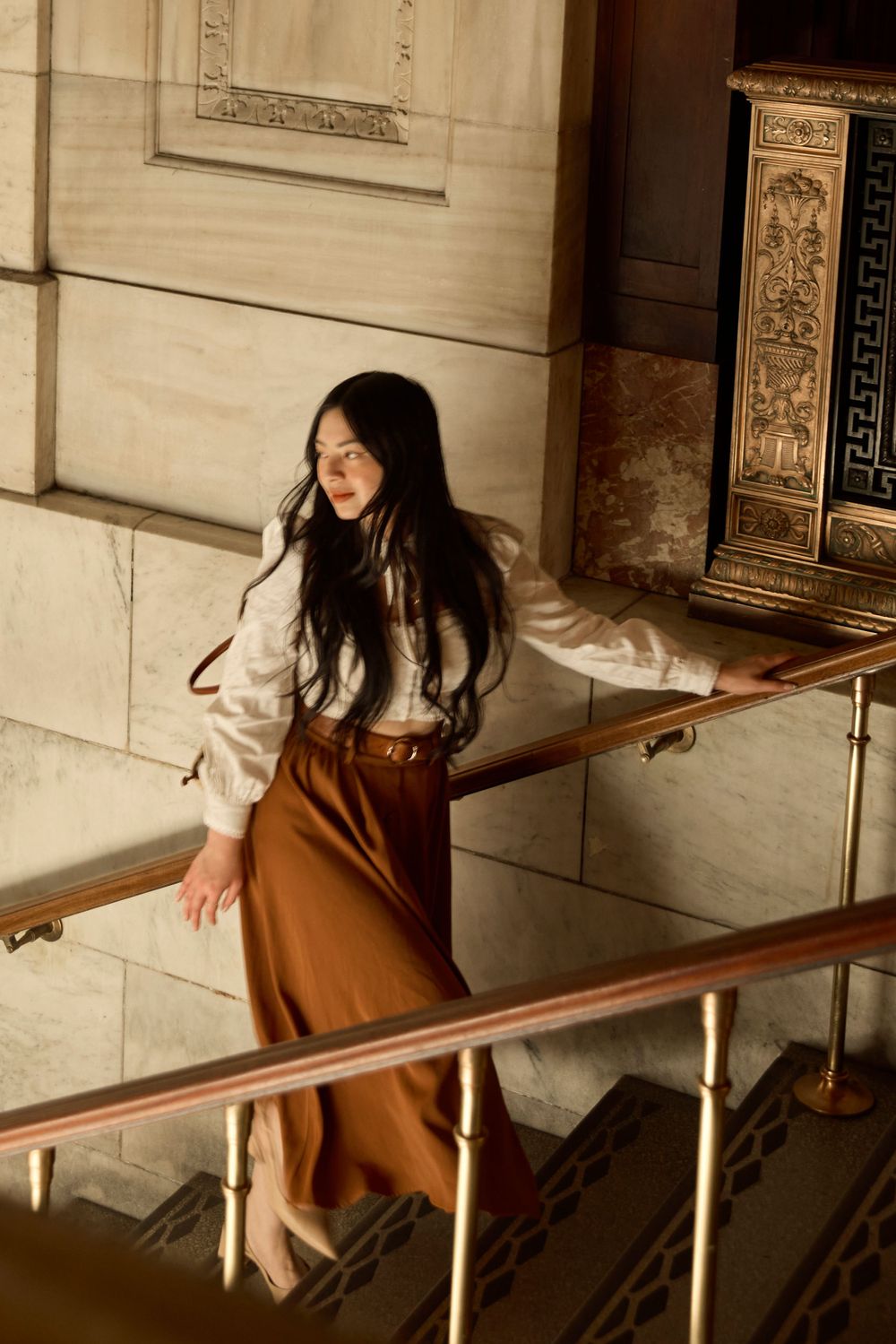 Person in vintage attire poses on elegant marble staircase in historic building.