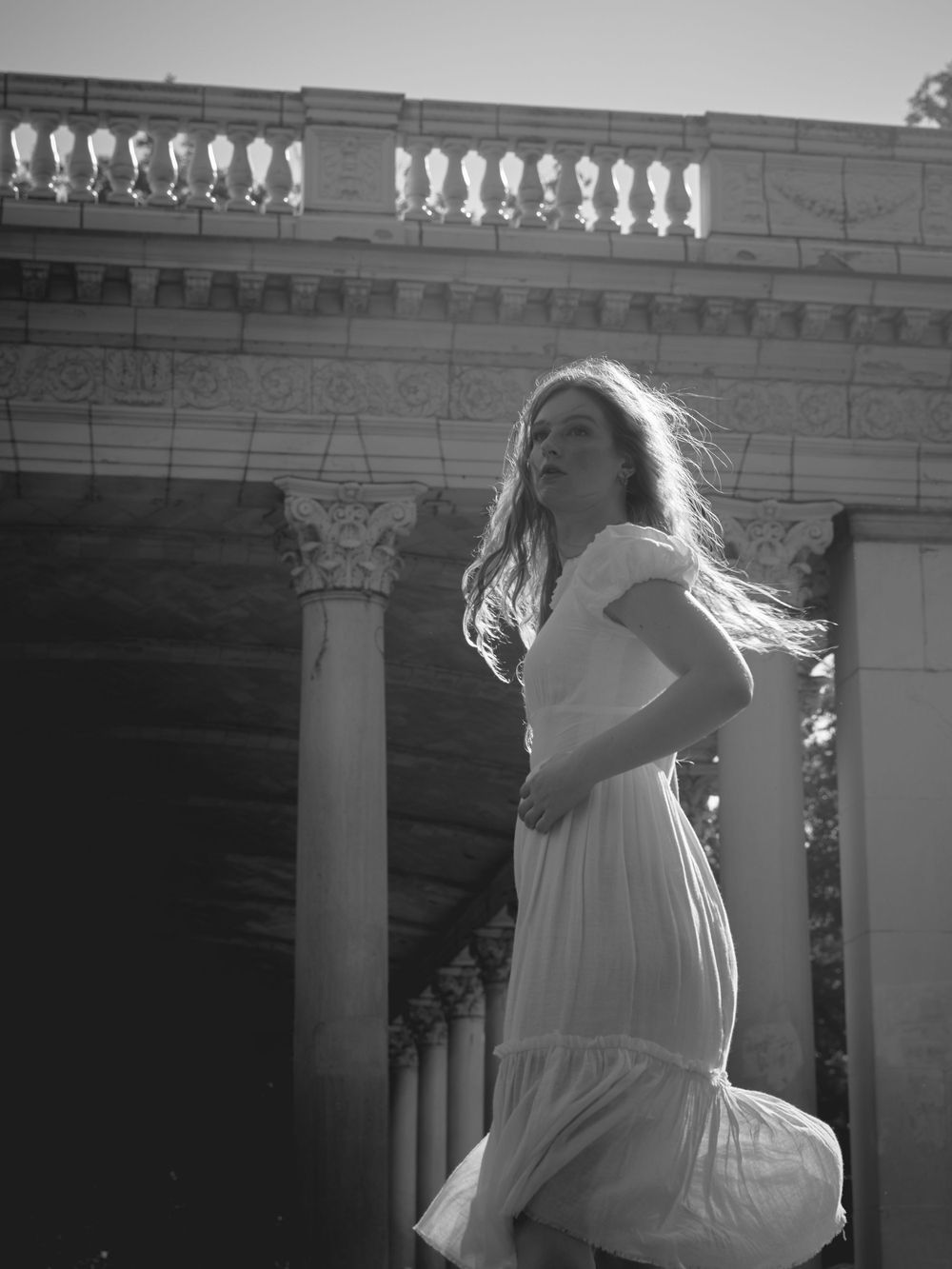 Black and white portrait with flowing dress against classical architecture and columns.