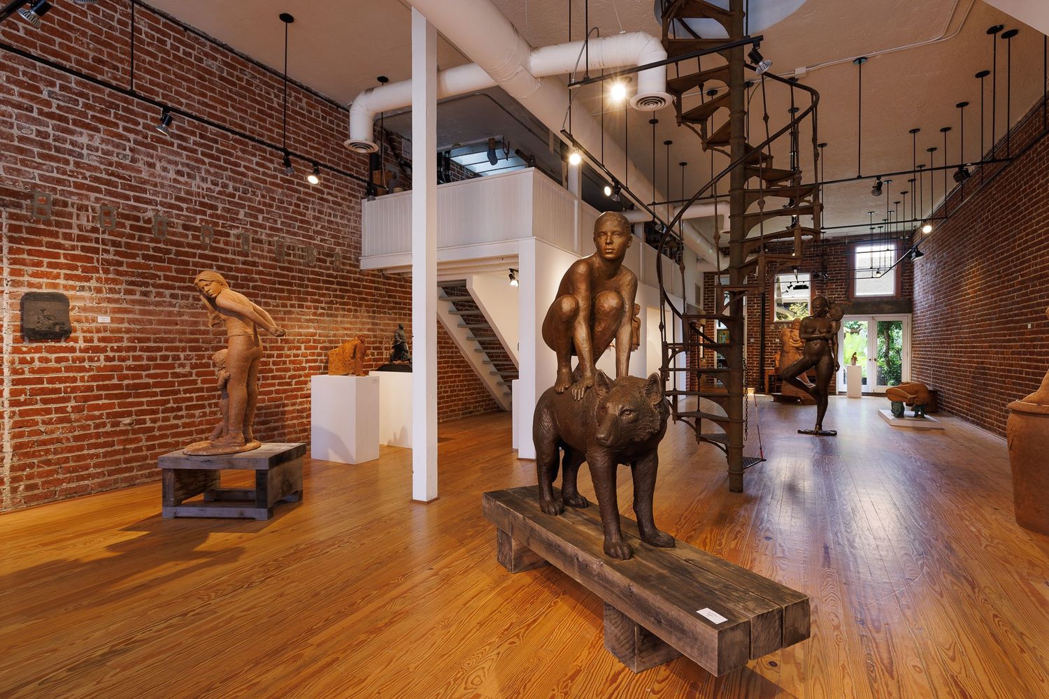 Industrial loft space with exposed brick walls featuring a large bronze horse statue and spiral staircase.