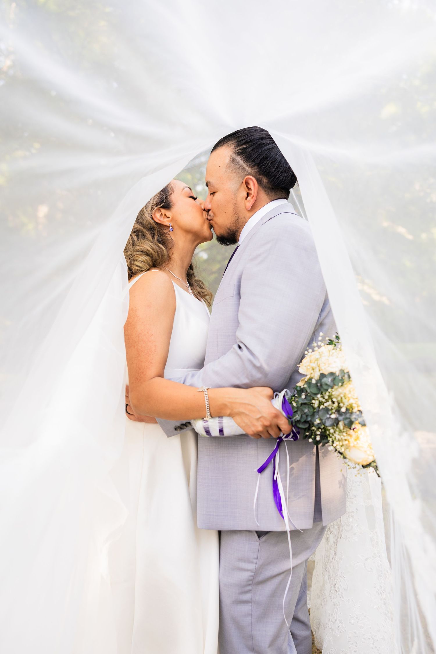 Romantic wedding moment captured with ethereal veil and sunlight effects.