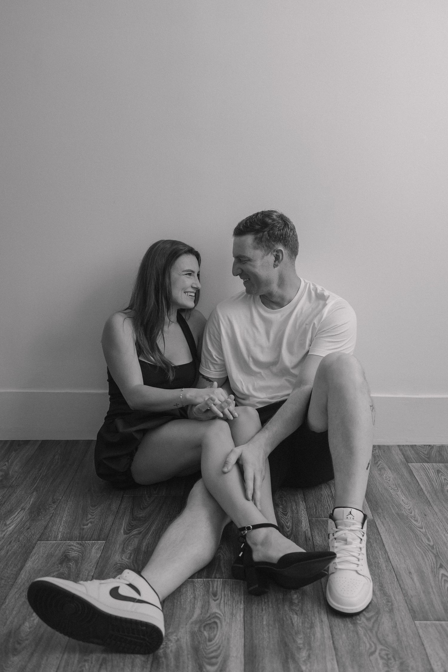 A couple sits together on a hardwood floor having an intimate conversation in black and white.