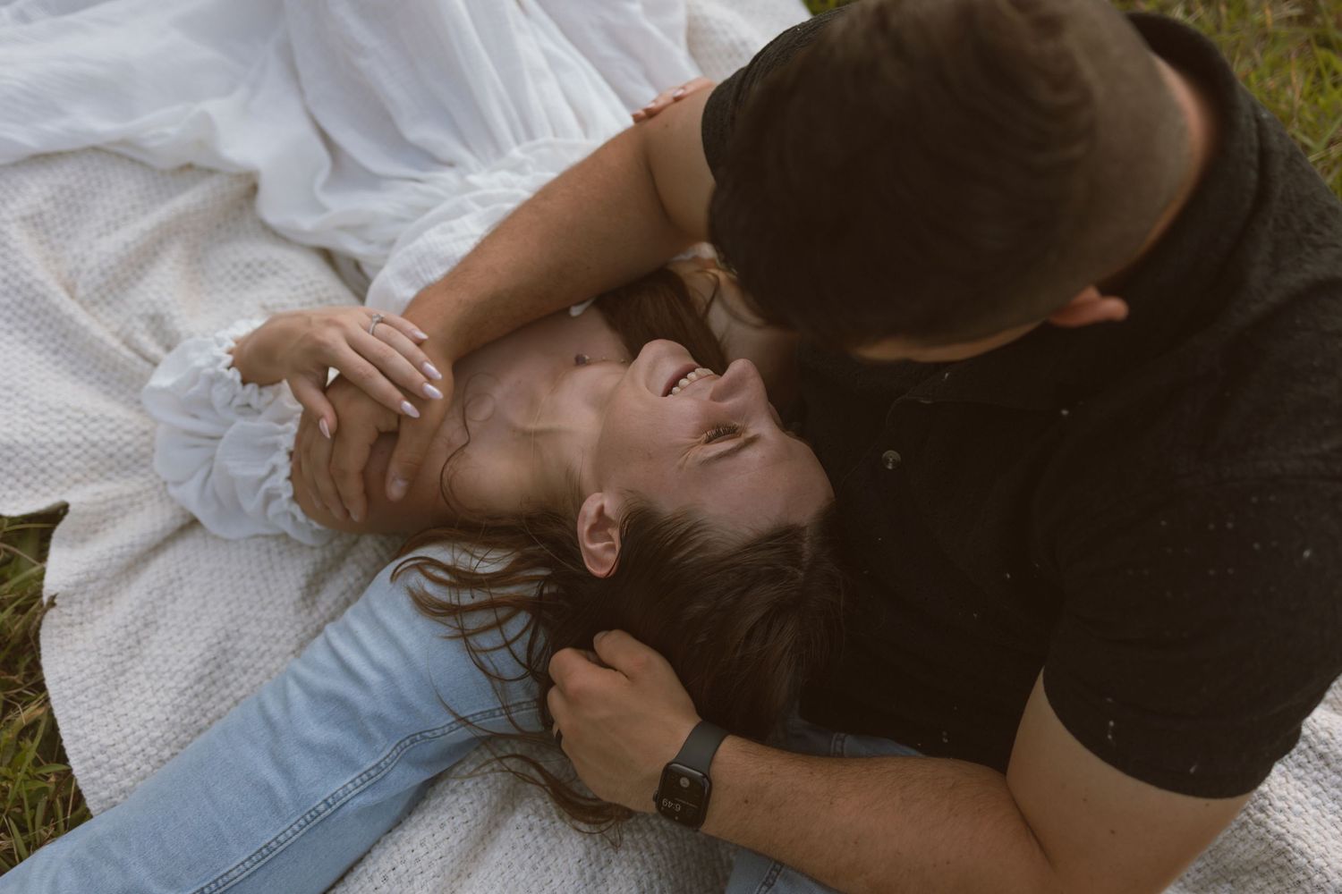 A romantic couple shares tender moments while lying in grass during a photo session.
