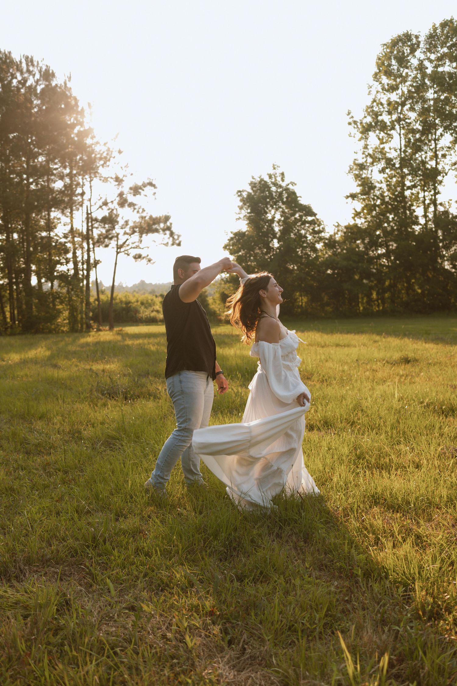 A couple dances playfully in a golden field during sunset.