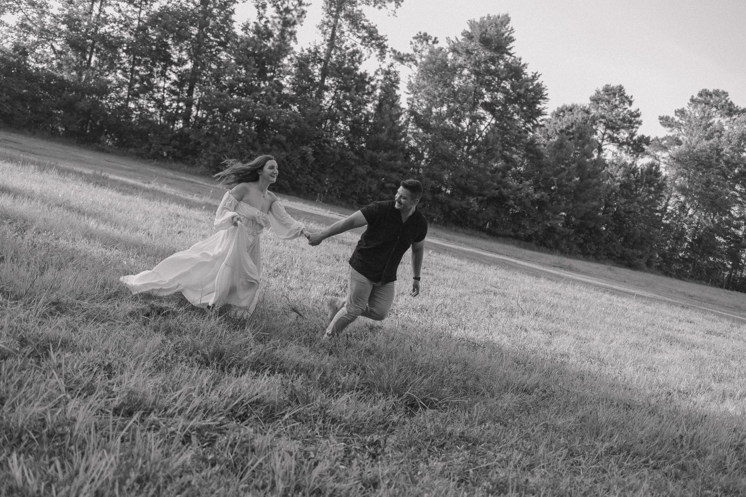 A couple in wedding attire runs playfully through an open field during their outdoor photo session.