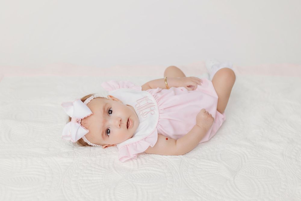 Baby in pink outfit lying on white backdrop during studio photoshoot.