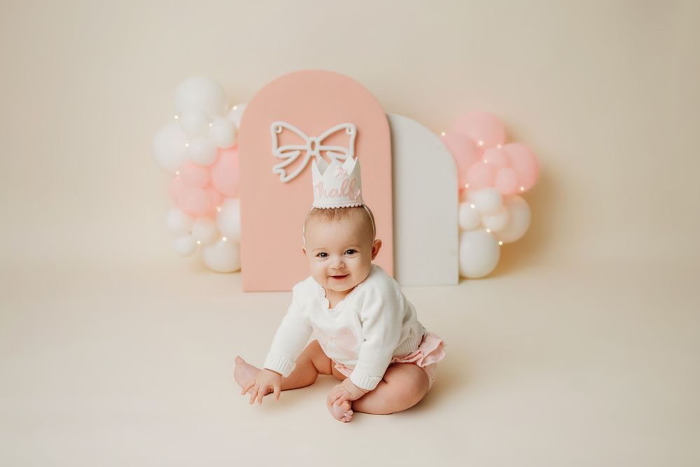 Studio portrait setup with pink arch backdrop and white balloon decorations.