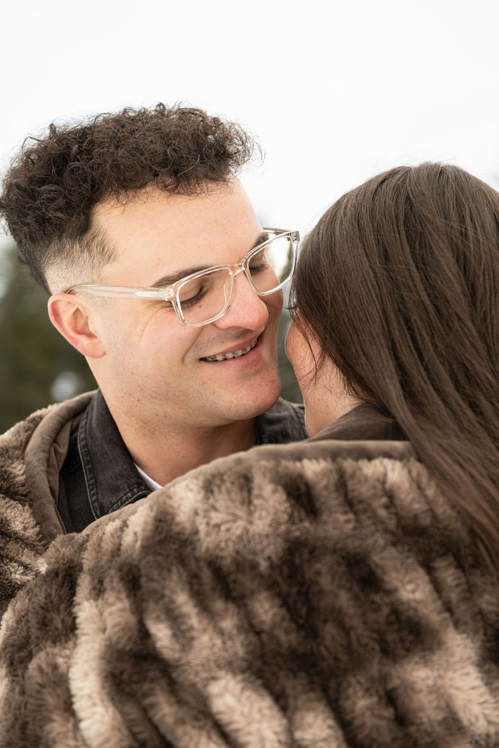A couple shares an intimate moment while wearing a blanket outdoor.