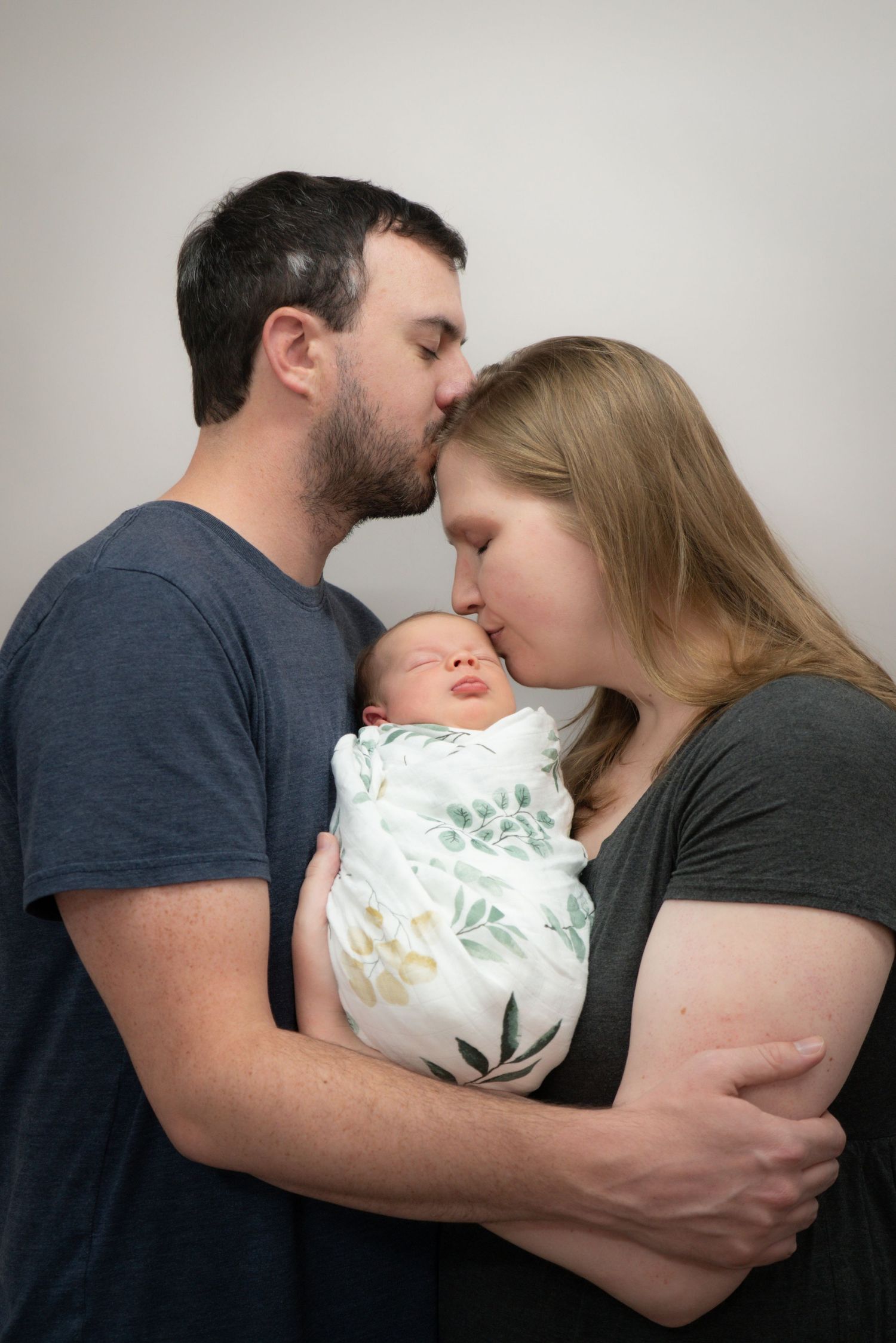 Intimate newborn portrait against black background in dramatic lighting.