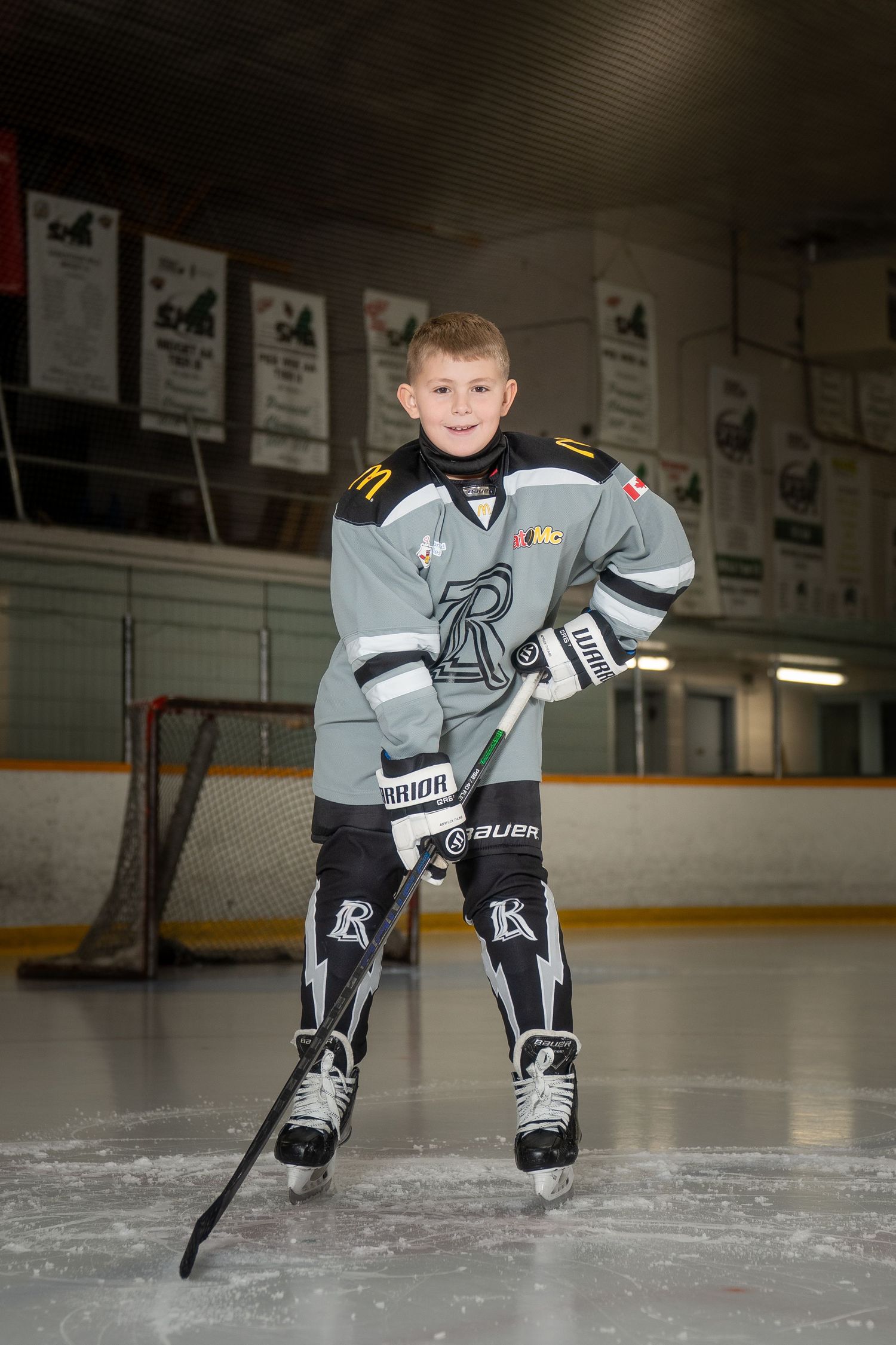 Young hockey player in gray jersey poses in a hockey position in an indoor ice rink.