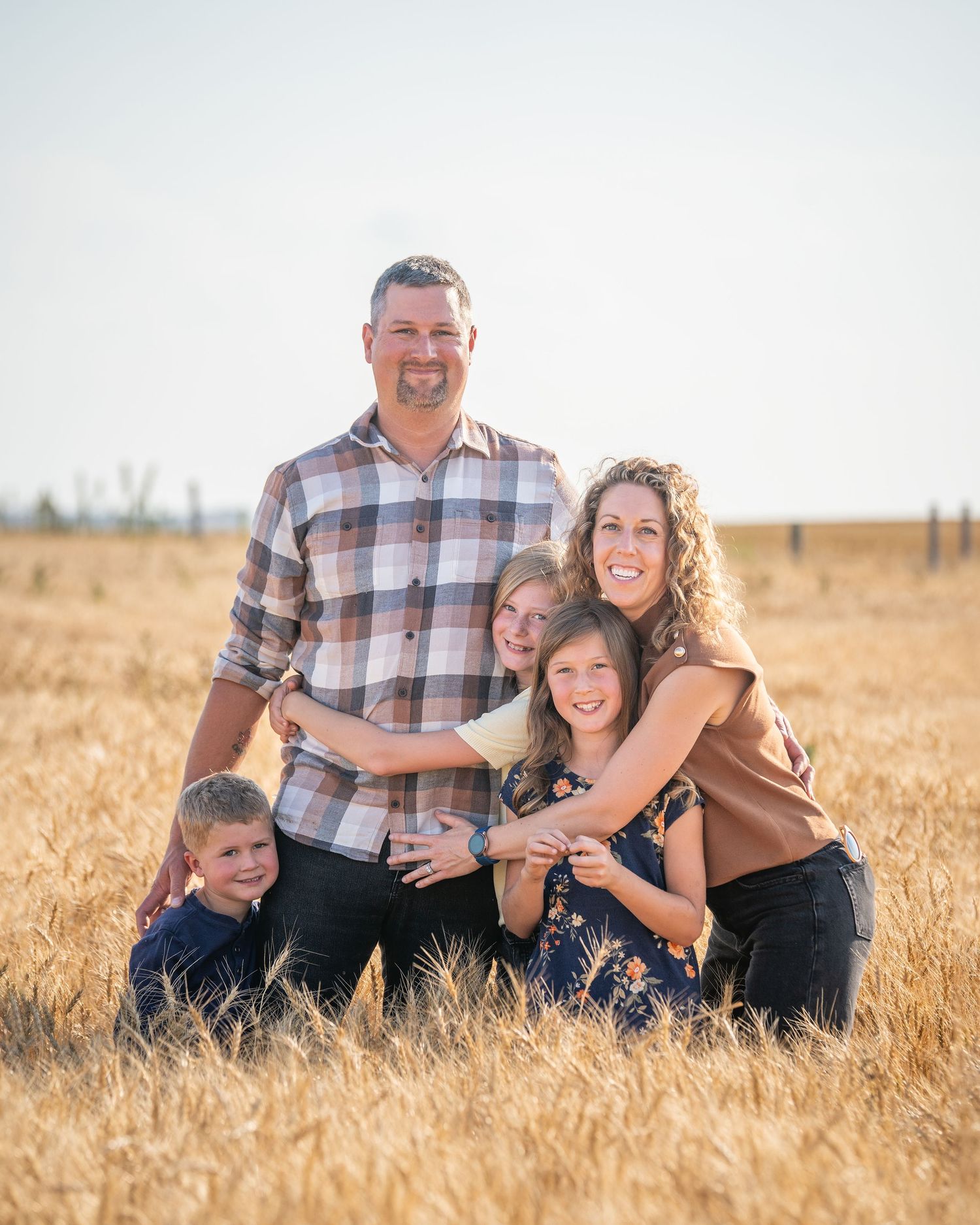 A family stands together in a golden wheat field during sunset, sharing joyful laughter and embraces.