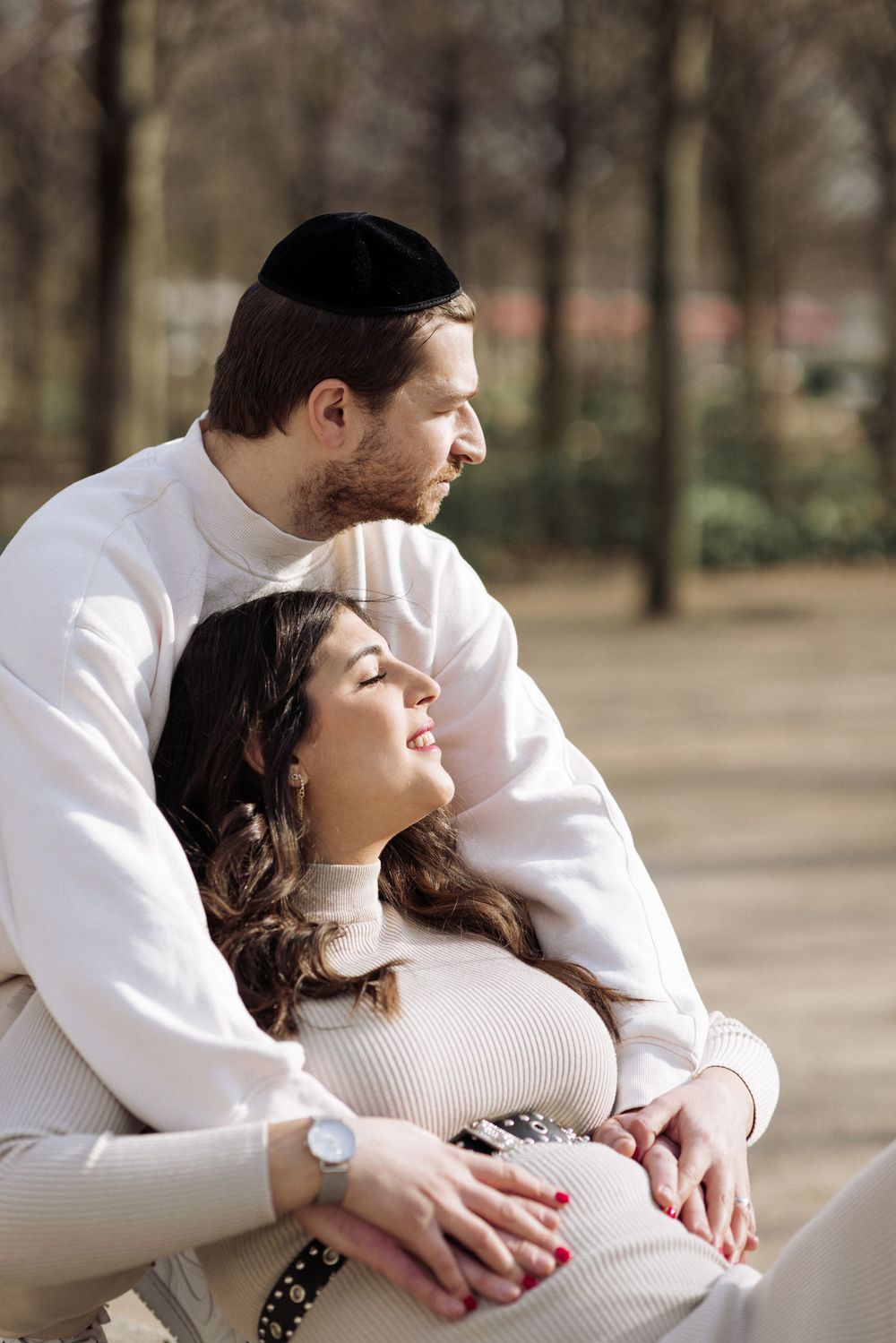 A couple embraces tenderly in a park setting during a maternity photo session.