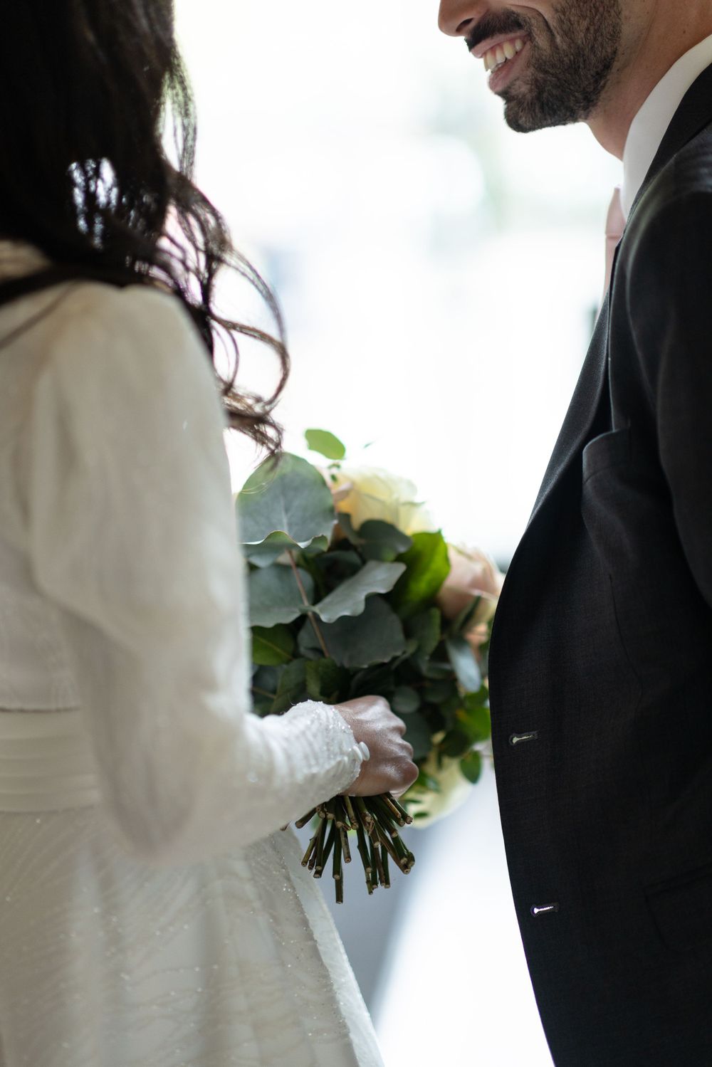 Close up of bride in white dress holding elegant bouquet with eucalyptus and roses.