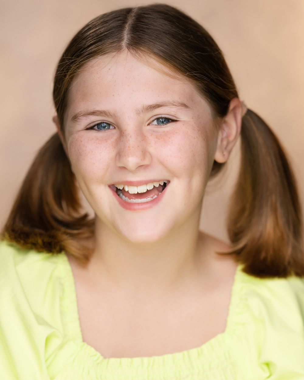 Cheerful person with pigtails wearing yellow top poses for headshot against warm background in Guildford, Surrey.