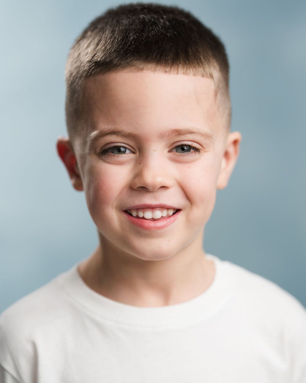 Portrait of smiling child in white t-shirt with short hair against light blue background. Headshots in Guildford, Surrey.