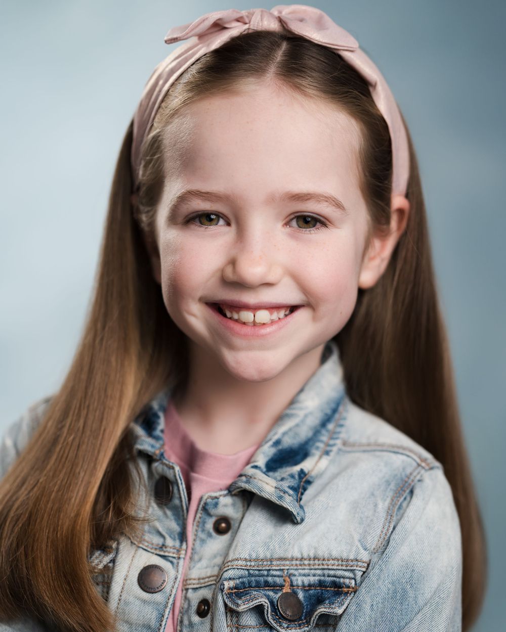 Studio portrait showing bright smile wearing denim jacket and pink headband. Children's headshots Surrey.