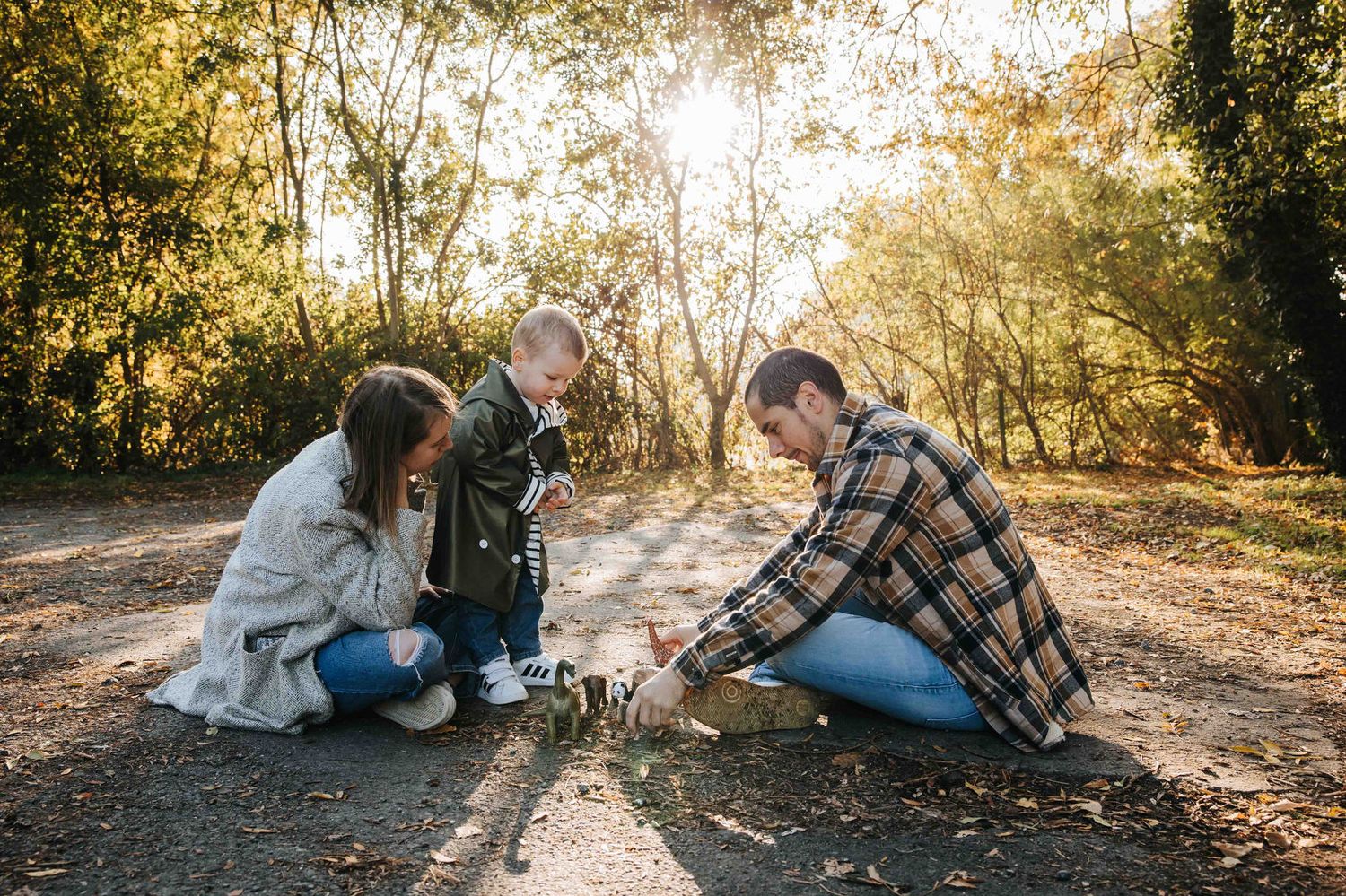 Group crouches on a sunlit autumn path in the woods while examining something on the ground together.