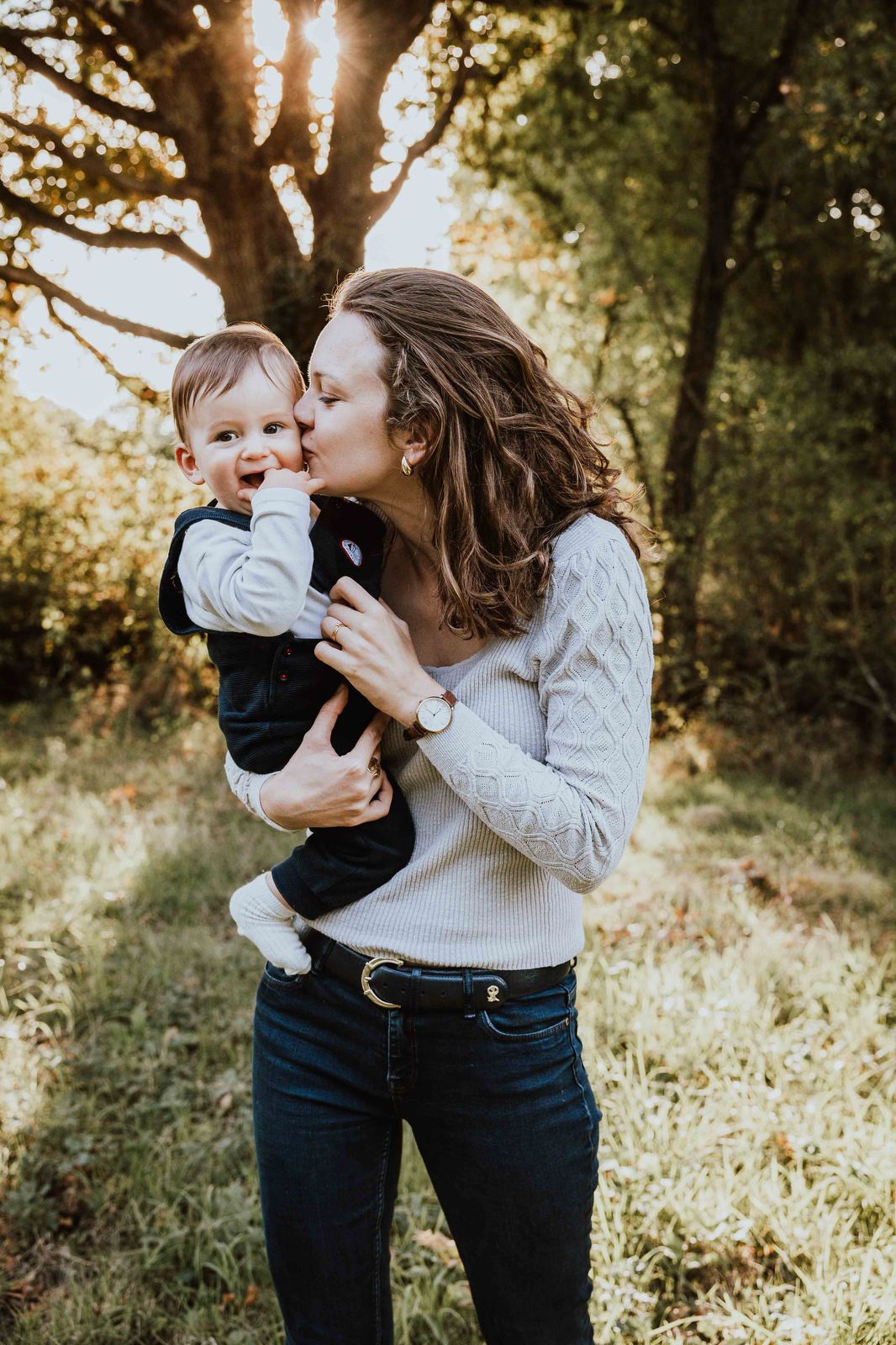 A tender outdoor family moment captured in golden sunlight through trees during an autumn photo session.
