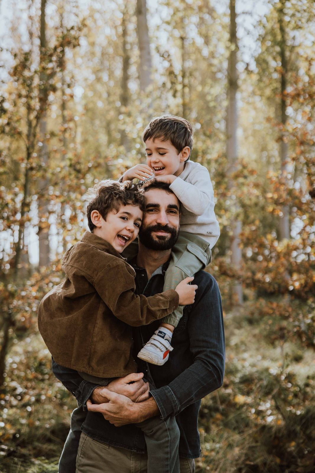 Joyful family moment captured in autumn woods with golden leaves and trees in background.