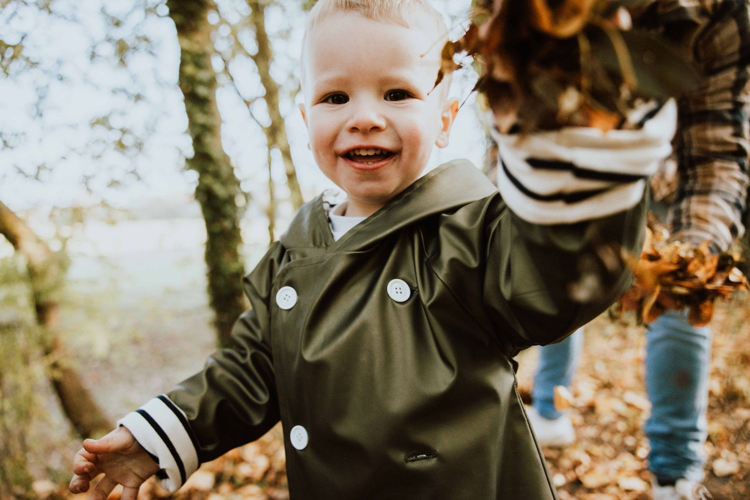 A toddler plays and smiles while exploring fallen autumn leaves in an outdoor setting.