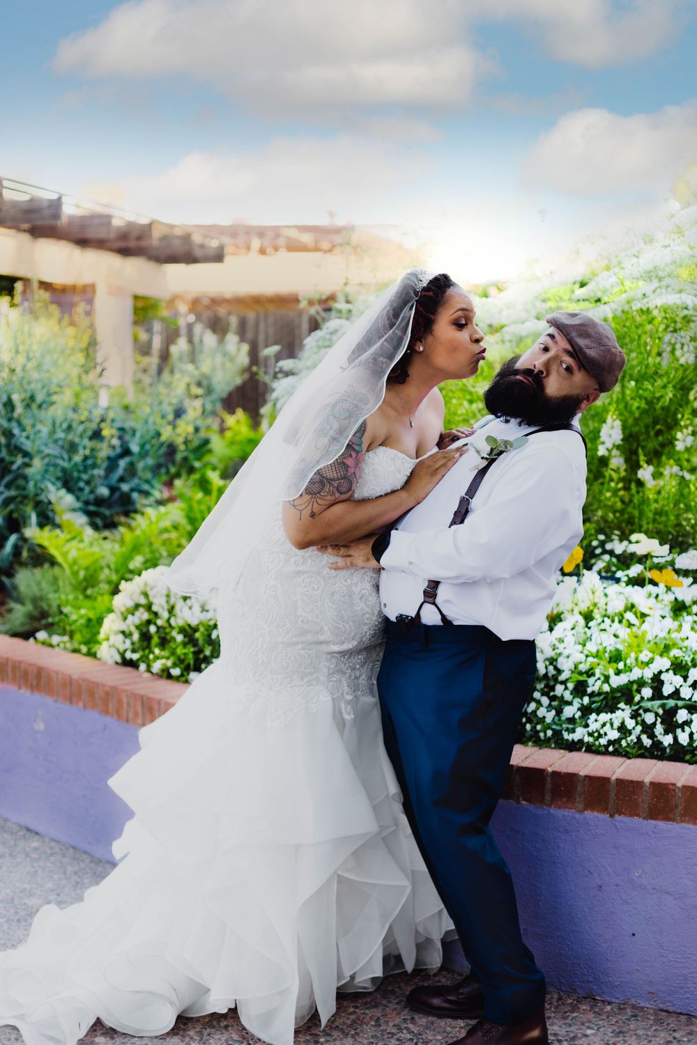 A couple shares a romantic moment in a garden setting with white flowers and greenery.