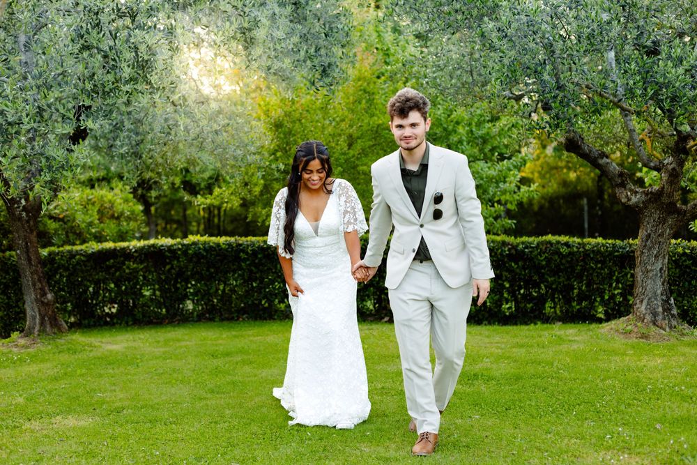 A bride and groom walk hand in hand through a lush garden setting during their outdoor wedding celebration.