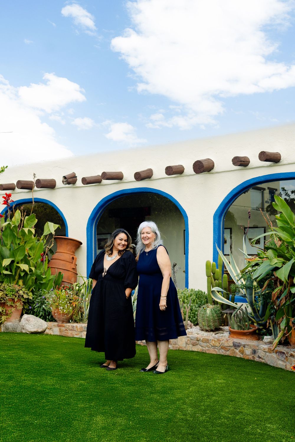 Guests gather outside a southwestern-style building with white walls, blue arches, and a lush green lawn.