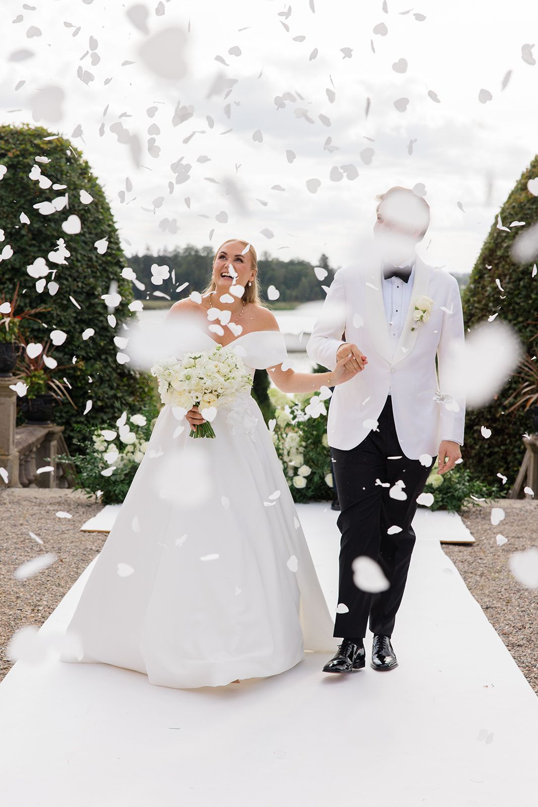 A joyful newlywed couple walks down the aisle while guests shower them with flower petals in black and white.