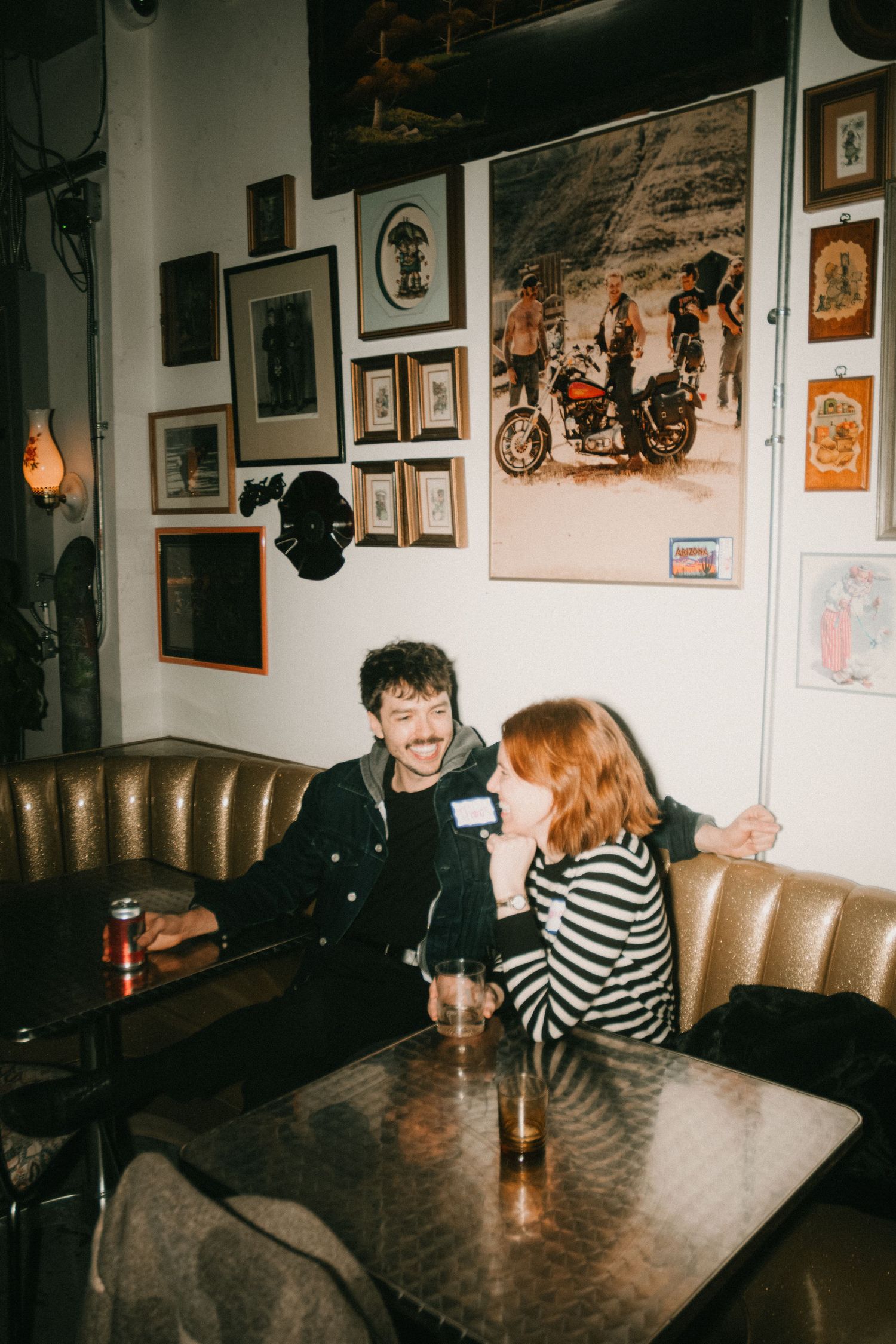 Two people sharing drinks and conversation in a bar with vintage photographs on walls.