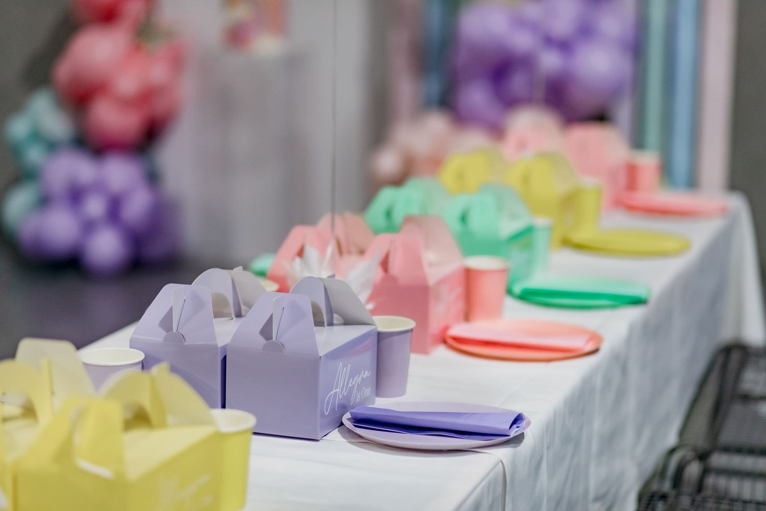 Colorful party favor boxes arranged in gradient colors from purple to yellow on a white tablecloth.