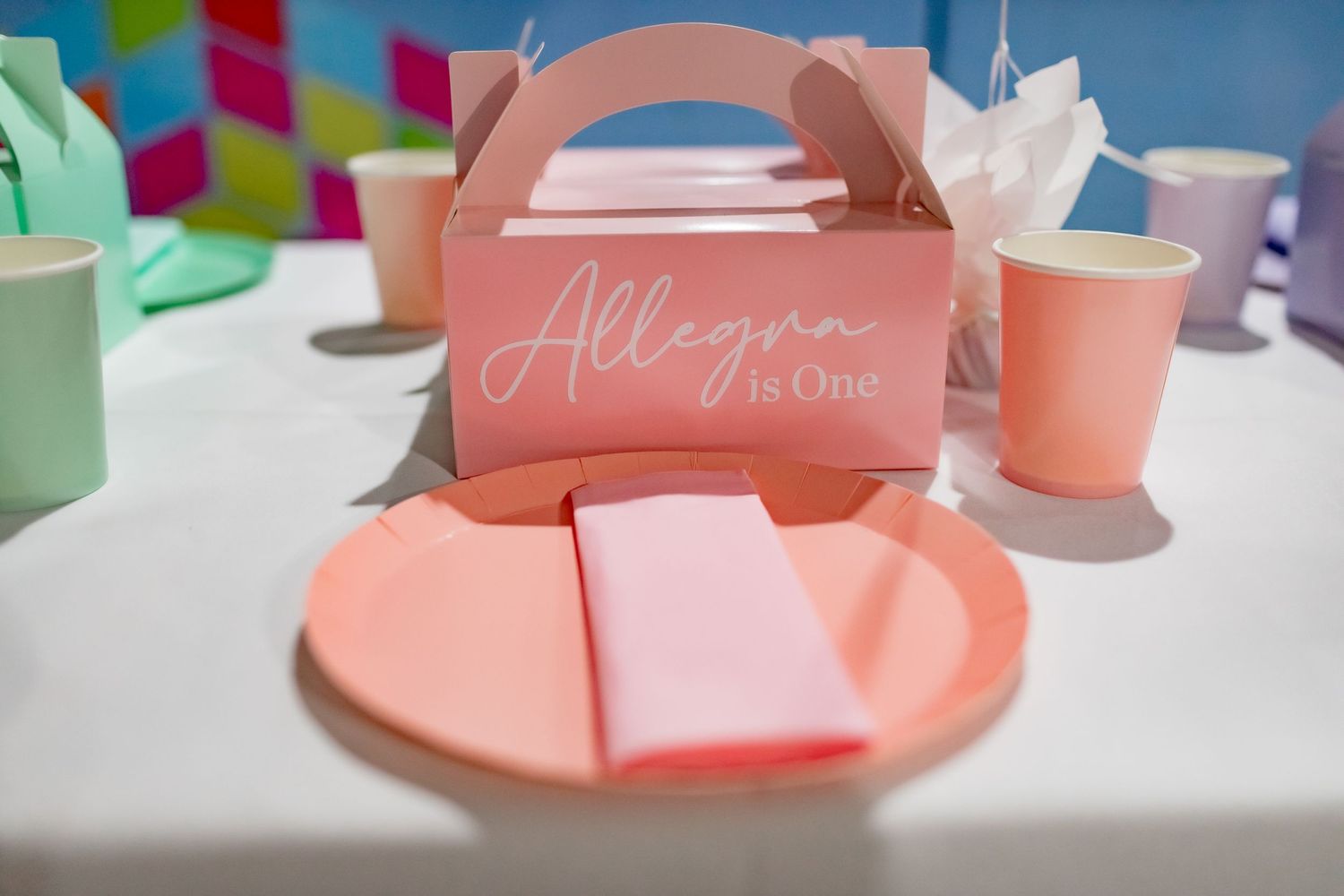 Pink party favor box with 'Allegra' text on white plates with matching cups.