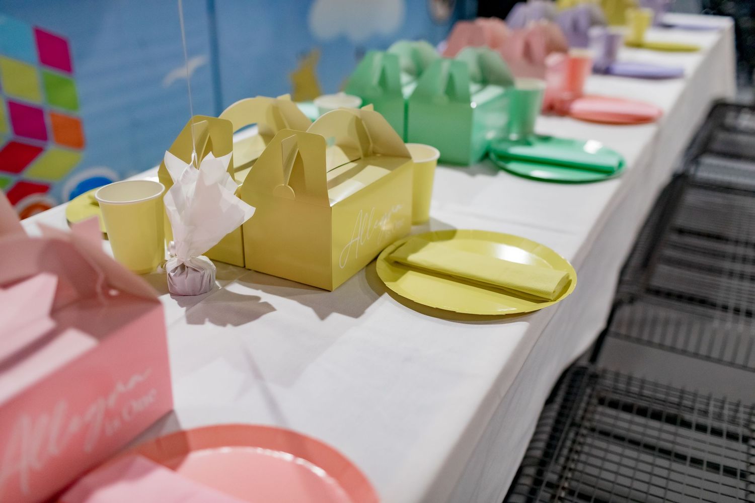 Gradient colored party favor boxes arranged on a white table with matching plates.