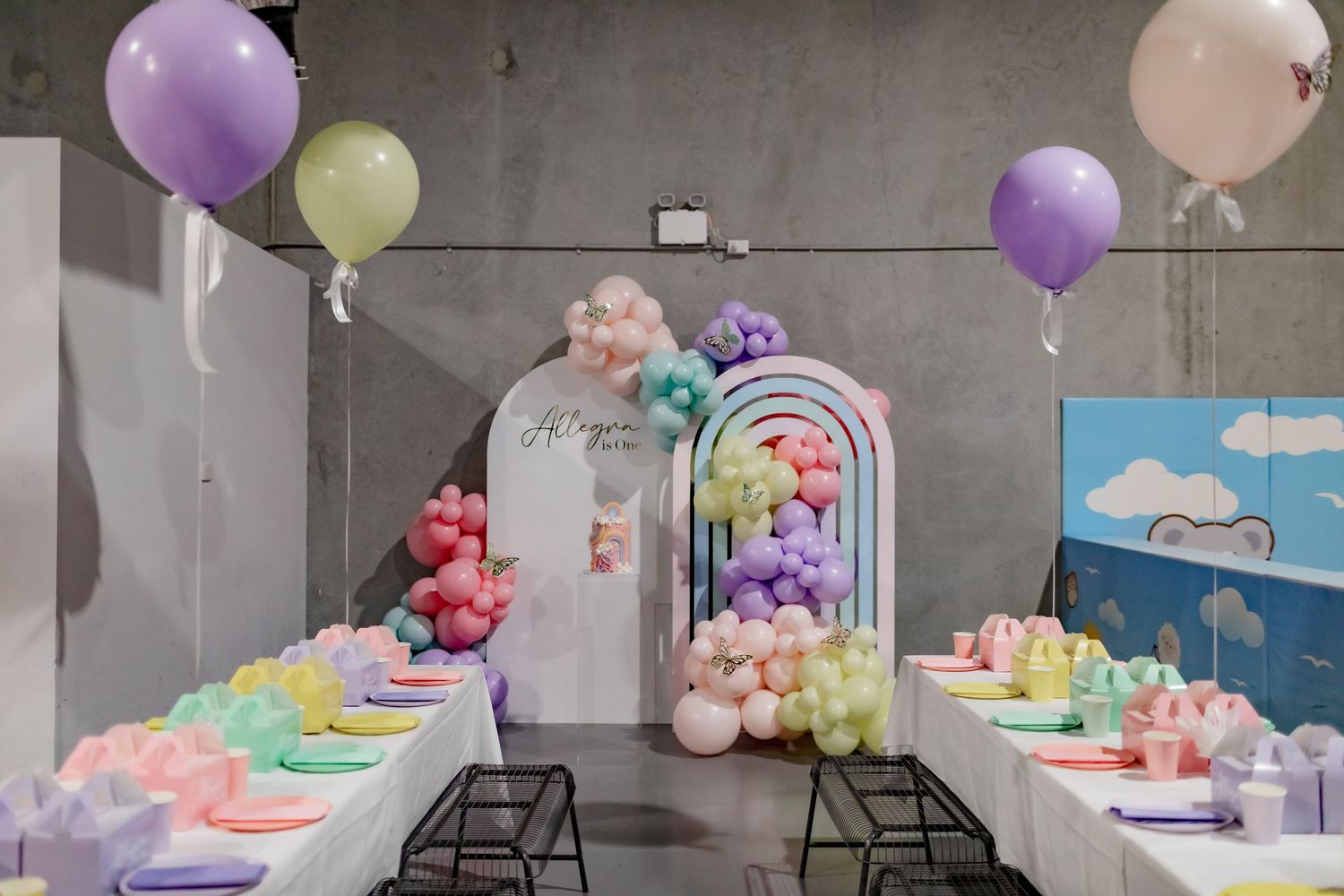 Pastel balloon arch and party decorations set up along tables with colorful place settings.