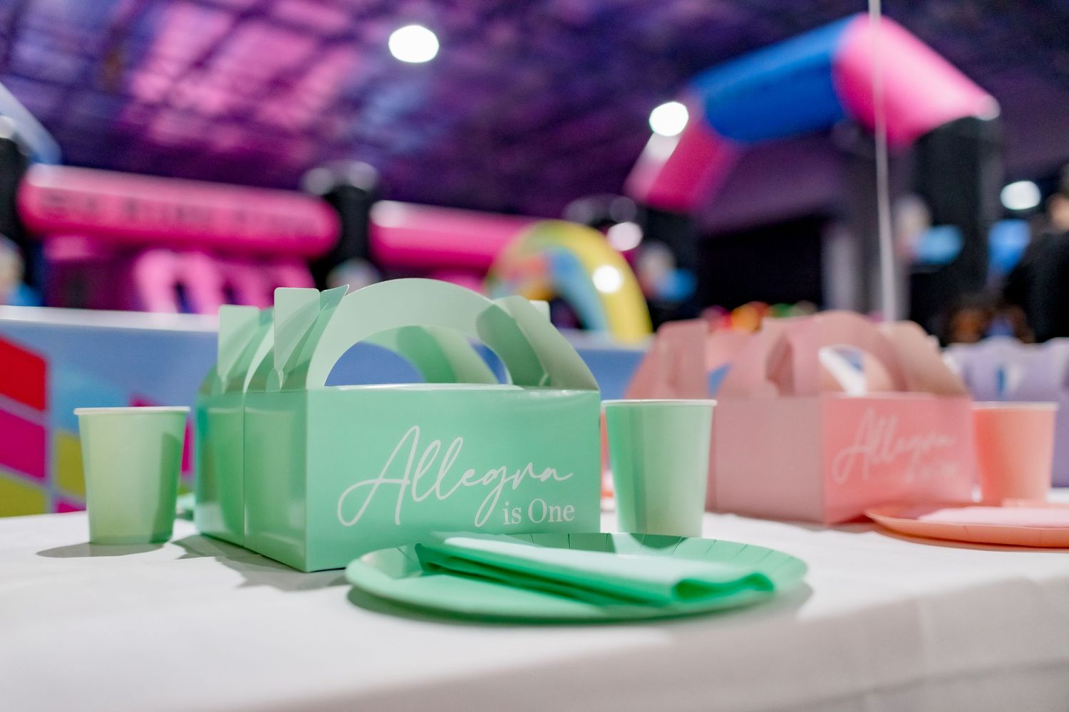 Colorful mint green and pink party place settings with cups and plates arranged on a table.
