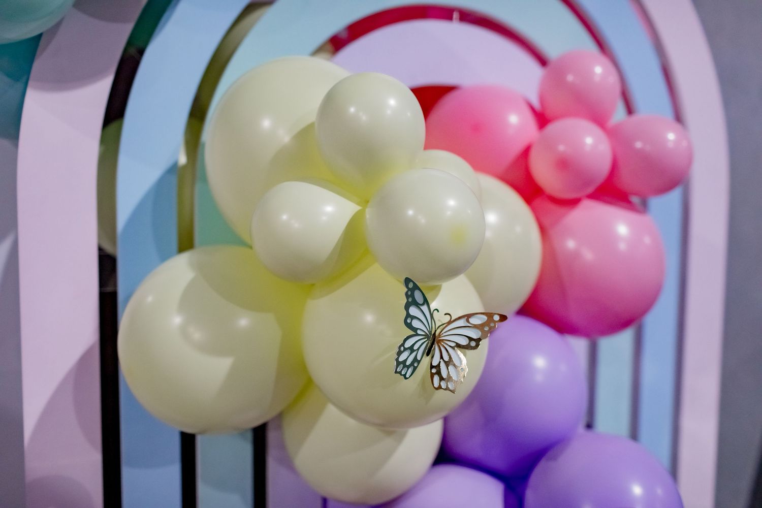 Pastel balloon arch with yellow, pink, and purple balloons decorated with a delicate butterfly accent.